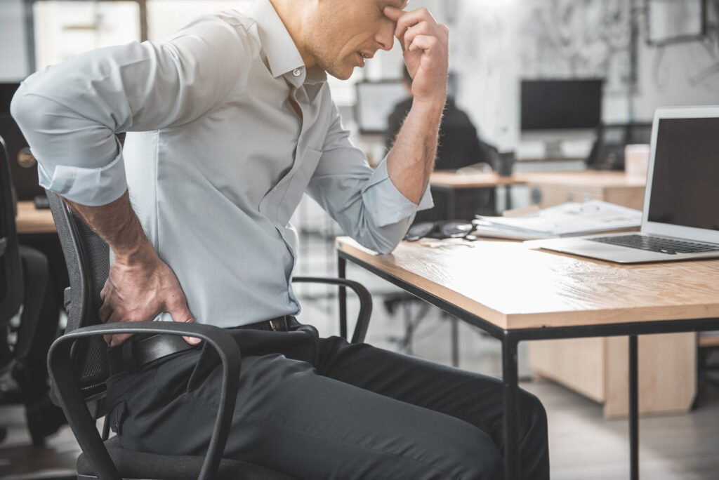 man in office holding his lower back due to pain